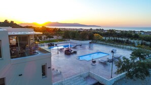 A rooftop pool area with lounge chairs, a hot tub, and a view of the sea at sunset. - LIBERTY &  FREEDOM villa, helipad and pools!Perfect for large groups up to 16 ! (Platanias)