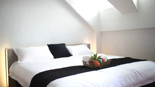 A neatly made bed with white linens, a black throw blanket, and a small basket of toiletries. - AgaPe Plus Home (Hengchun)