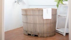 A wooden barrel with a towel hanging on it, placed on a tiled floor next to a white shelf and a plant. - AgaPe Plus Home (Hengchun)