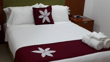 A neatly made bed with white and maroon bedding, a green headboard, and a white pillow with a maroon flower design.