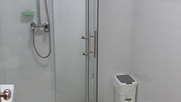 A bathroom with a glass-enclosed shower, a toilet, and a small trash bin.