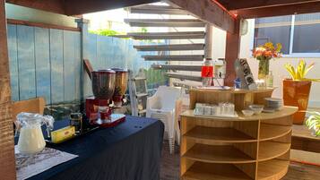 Una terraza de madera con una estación de café, un dispensador de agua y un pequeño rincón de estar con mesa y sillas.