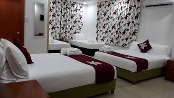 Habitación de hotel con dos camas individuales, cada una con ropa de cama blanca y una colcha floral roja. Hay una mesita de noche de madera con una lámpara, y las cortinas de la habitación tienen un estampado floral rojo y gris.