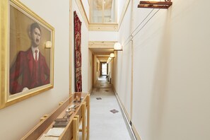 A narrow hallway with a wooden bench, a framed portrait, and a patterned curtain.