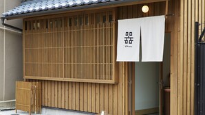 A traditional Japanese building with wooden slats, a white sign with Japanese characters, and a small wooden stool outside. - utsuwa Designed Hostel (Kyoto)