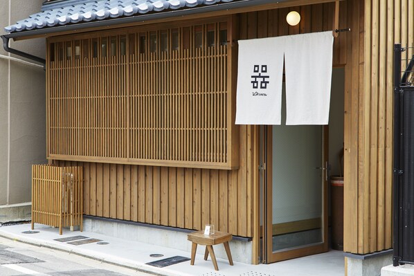A traditional Japanese building with wooden slats, a white sign with Japanese characters, and a small wooden stool outside.