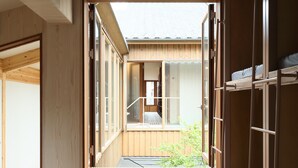 A narrow corridor with wooden walls and floors, leading to a room with a bed and a window. - utsuwa Designed Hostel (Kyoto)