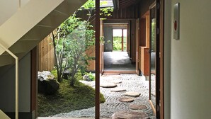 A modern interior with a concrete staircase, a wooden door leading to a garden, and a view of a traditional building. - utsuwa Designed Hostel (Kyoto)