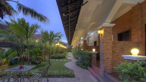 A courtyard with a brick wall, a paved walkway, and outdoor seating. - My Unique Angkor Siemreap (Siem Reap)
