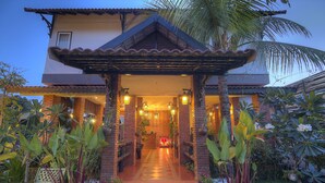 A building with a covered entrance, brick walls, and a tiled pathway leading to a central area with a decorative light fixture. - My Unique Angkor Siemreap (Siem Reap)