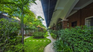 A pathway flanked by lush greenery and a brick building with arched windows. - My Unique Angkor Siemreap (Siem Reap)
