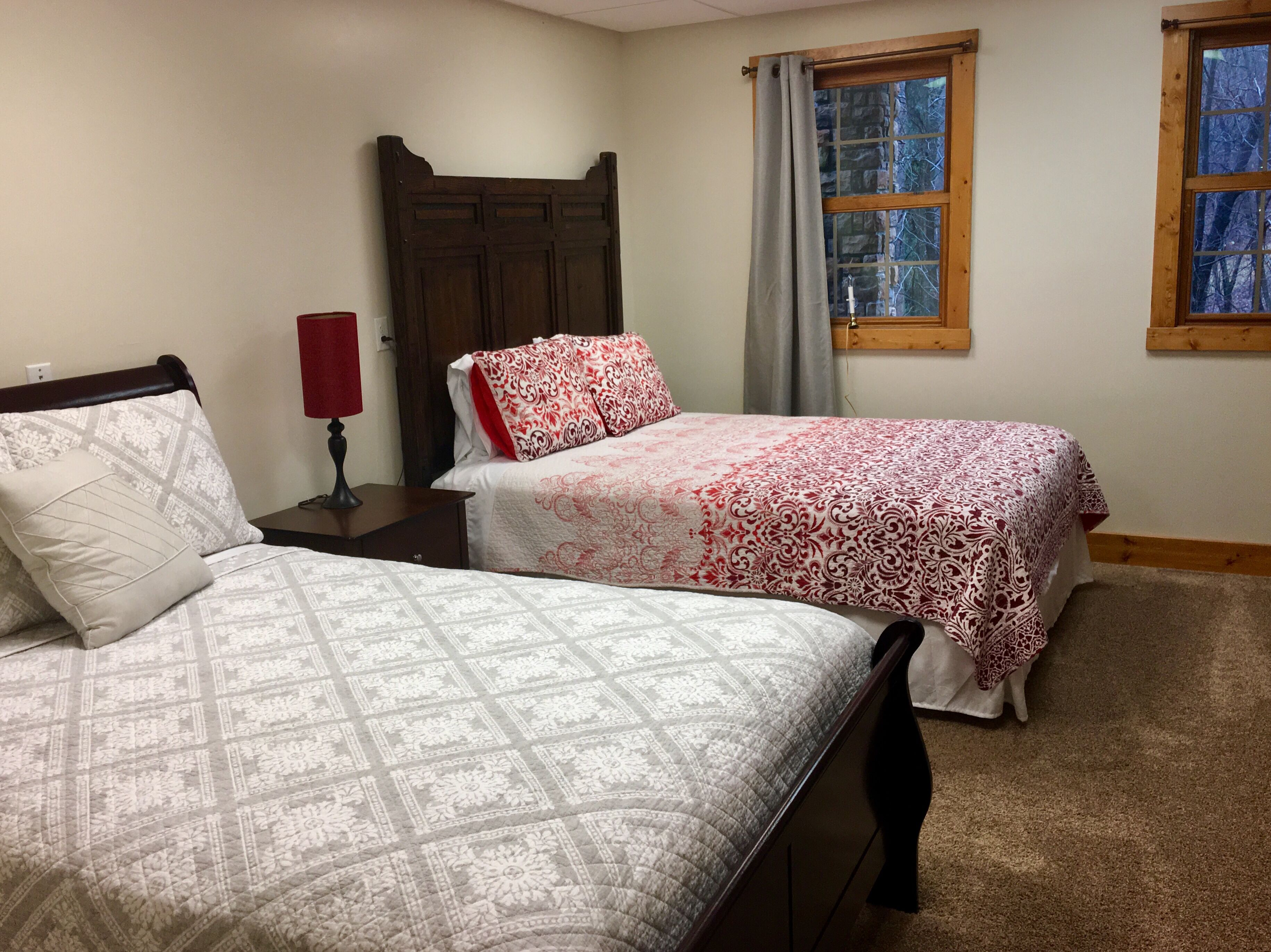 A bedroom with two beds, a nightstand, a lamp, and a window with curtains.