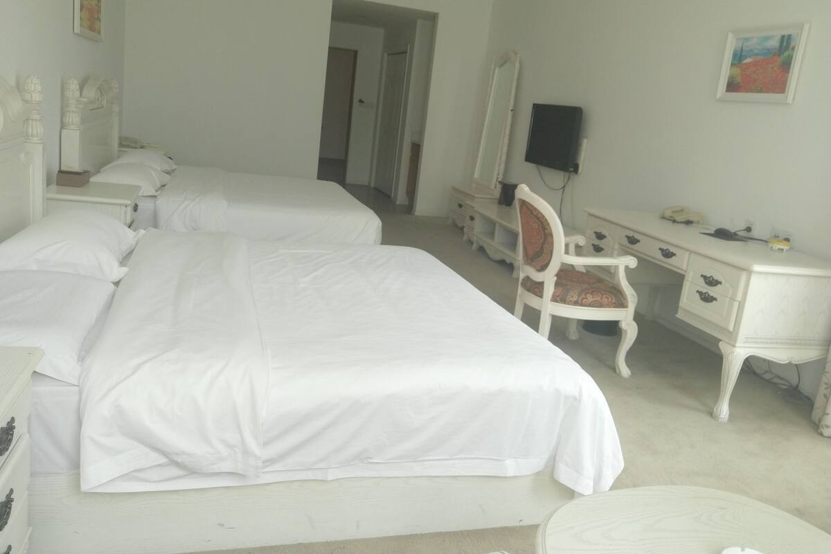 Ein Hotelzimmer mit zwei Betten, einem Schminktisch, einem Sessel und einem Fernseher.