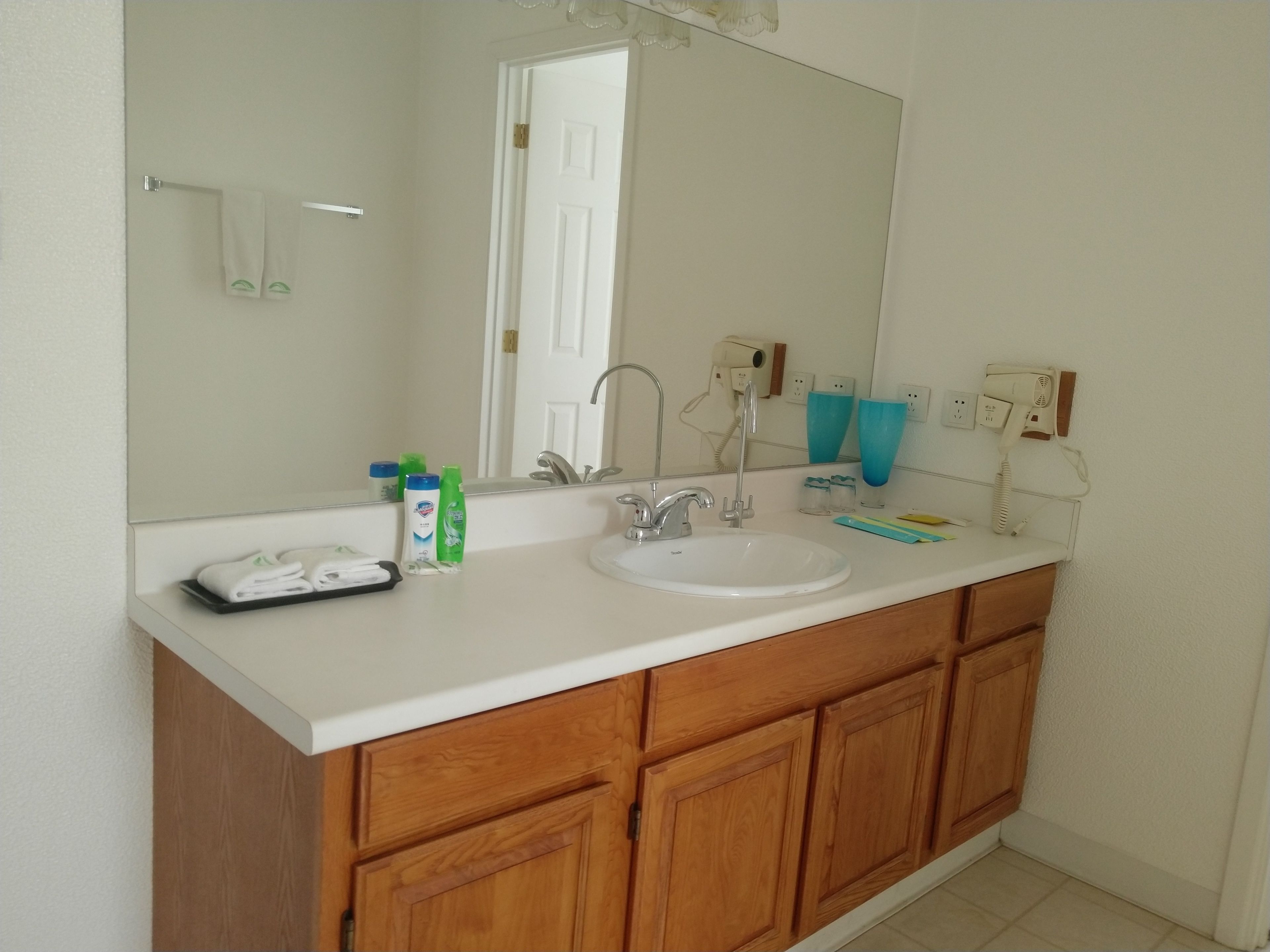 Een badkamer met een wit wastafel, houten kastjes, een spiegel en toiletartikelen op het aanrecht.