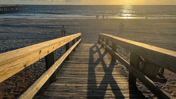 A wooden pier leading to a beach with the sun setting in the background. - Oleander - Charming Cottage Downtown - Steps to the Beach! (Flagler Beach)