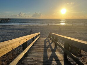 Un moll de fusta que condueix a una platja amb el sol ponent-se al fons.