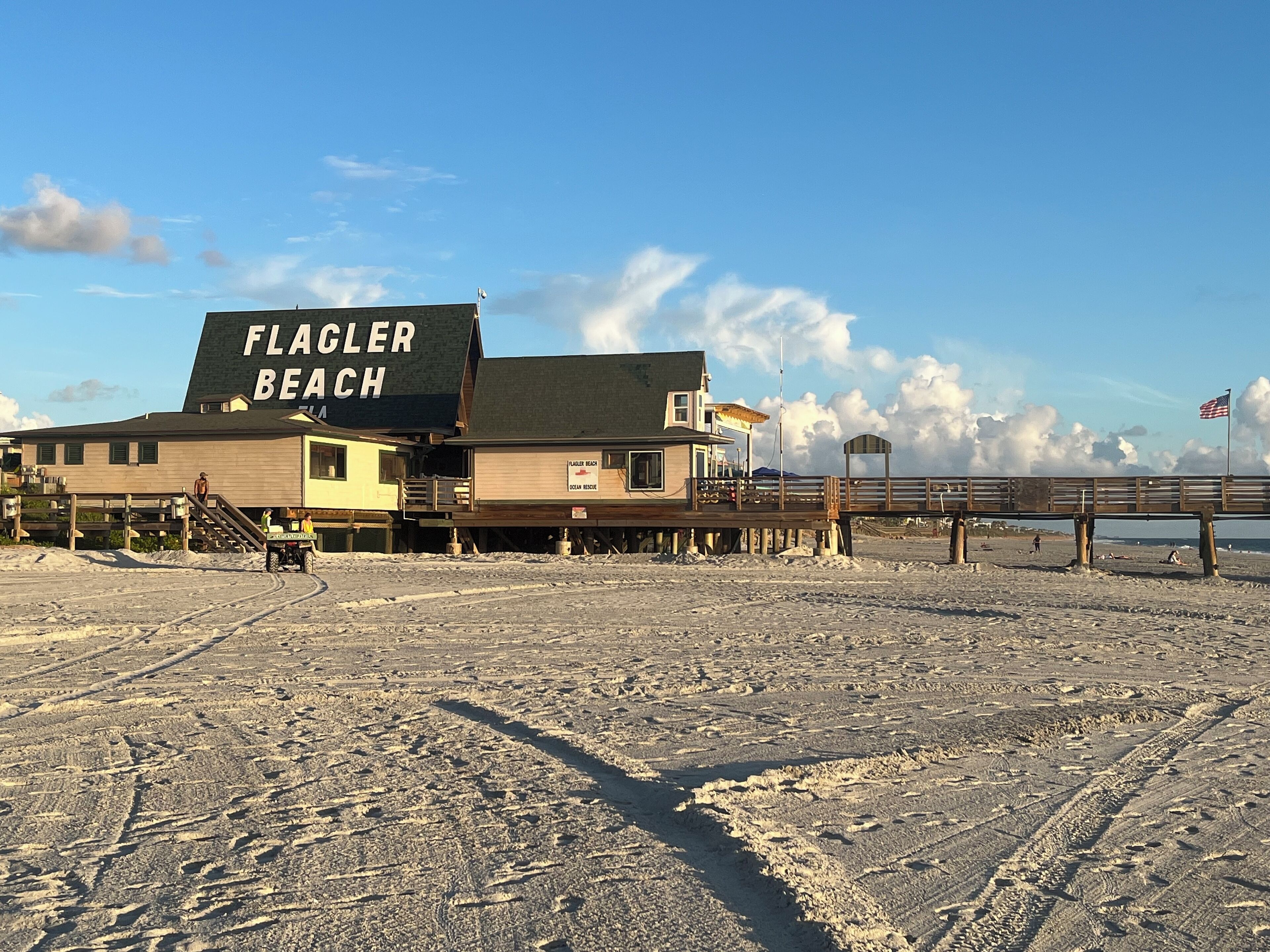 Une maison de plage appelée « Flagler Beach », dotée d’une terrasse en bois et d’une jetée qui s’avance dans l’océan.