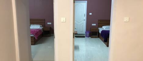 A hallway leading to two bedrooms, each with a bed, nightstand, and a door.