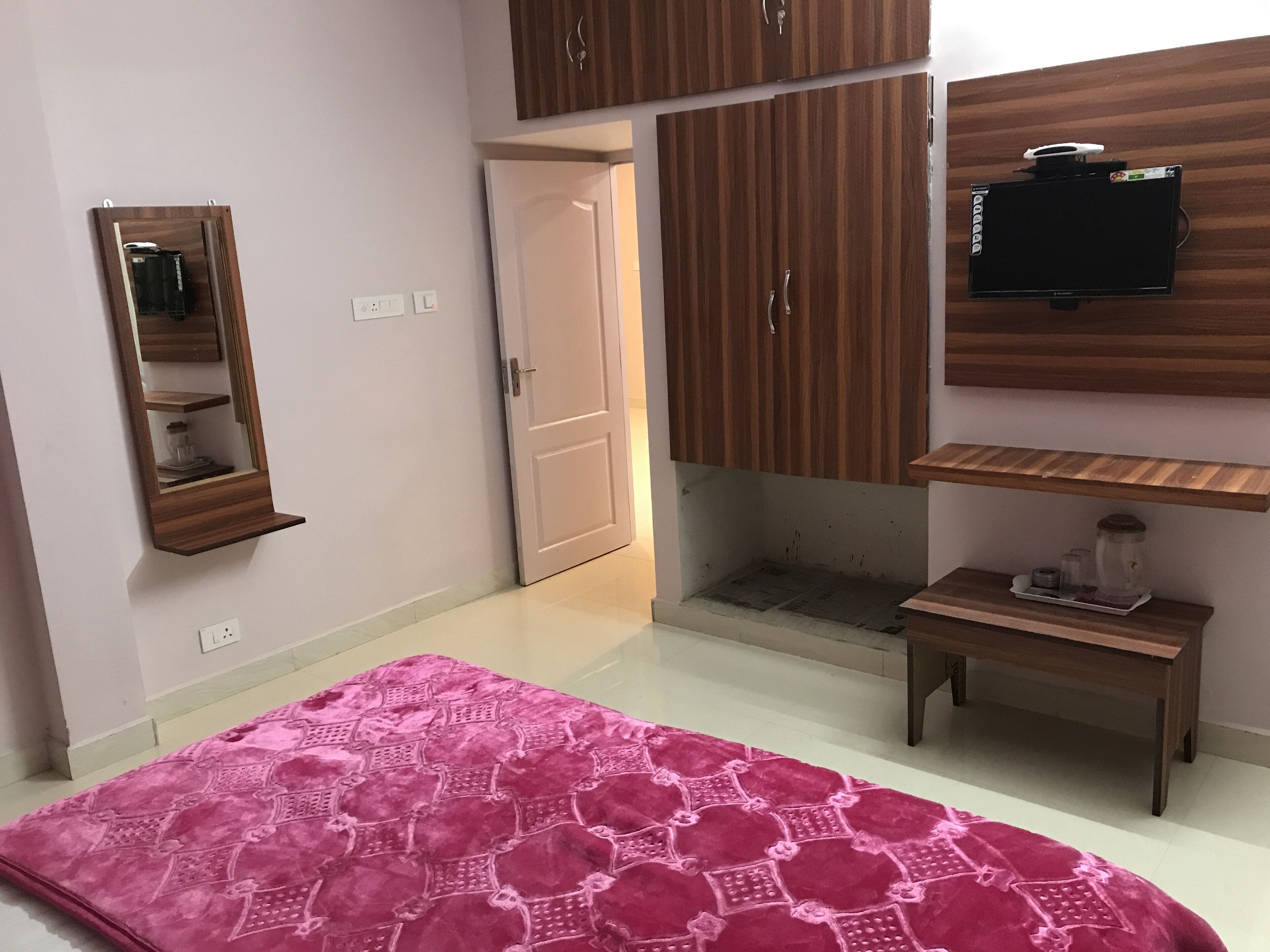 A room with a pink patterned rug, wooden cabinets, a TV mounted on the wall, and a small wooden table with a glass jar.