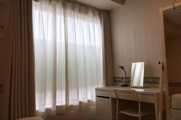 A hotel room with a desk, chair, and a large window with curtains.