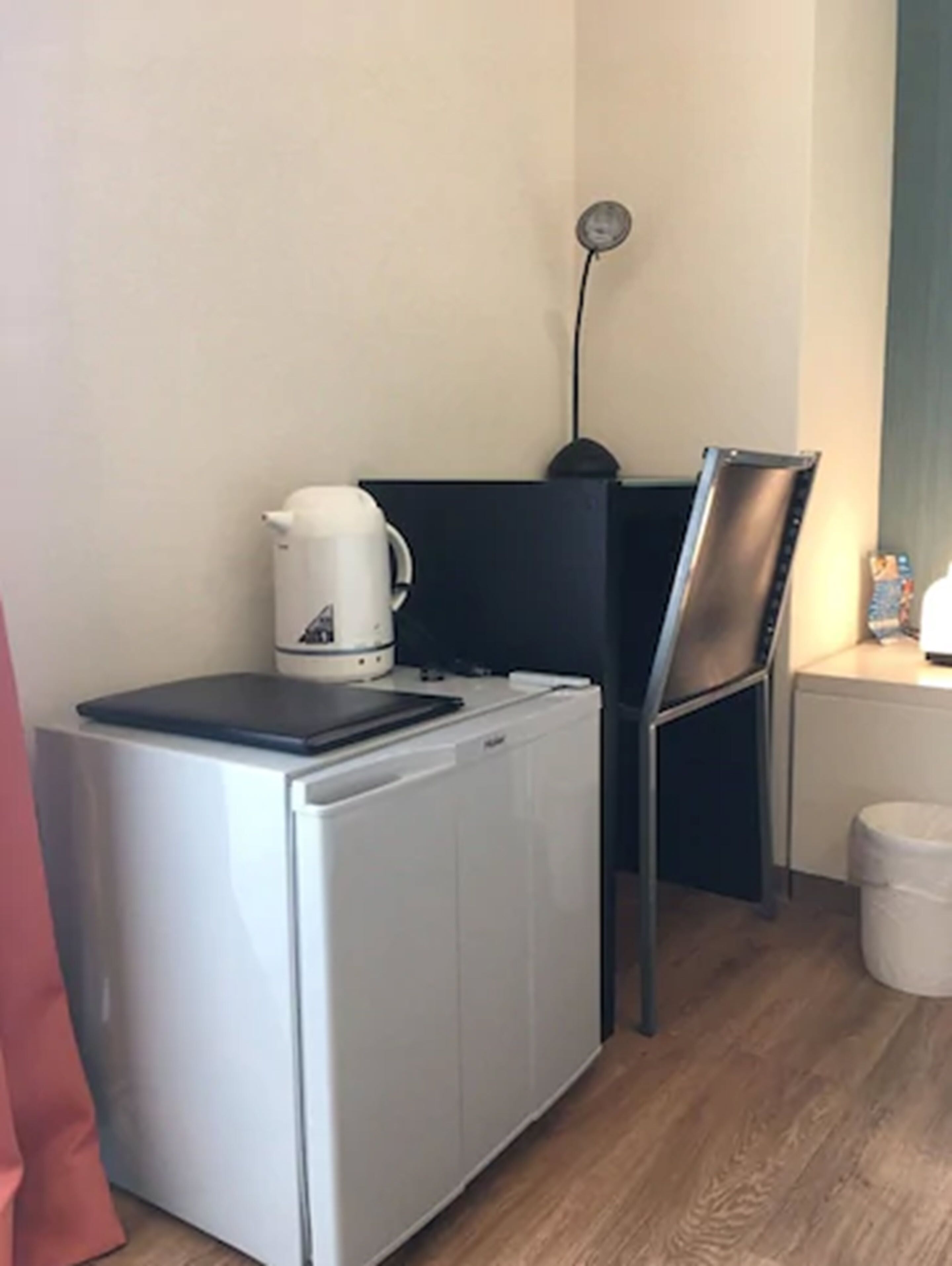 A compact kitchenette with a coffee maker, a small refrigerator, a chair, and a lamp.