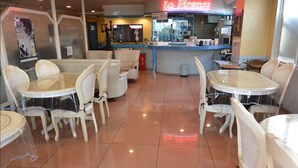 A restaurant interior with round tables and chairs, a kitchen area, and a neon sign. - BUSINESS HOTEL La Firenze (Tokyo)