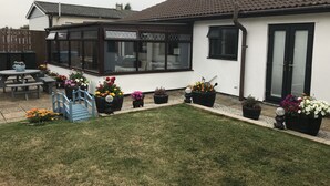 A house with a conservatory, a patio with a table and chairs, and a variety of potted plants. - The Batch, 5* Self Catering Bungalow, St Merryn Padstow (St Merryn)