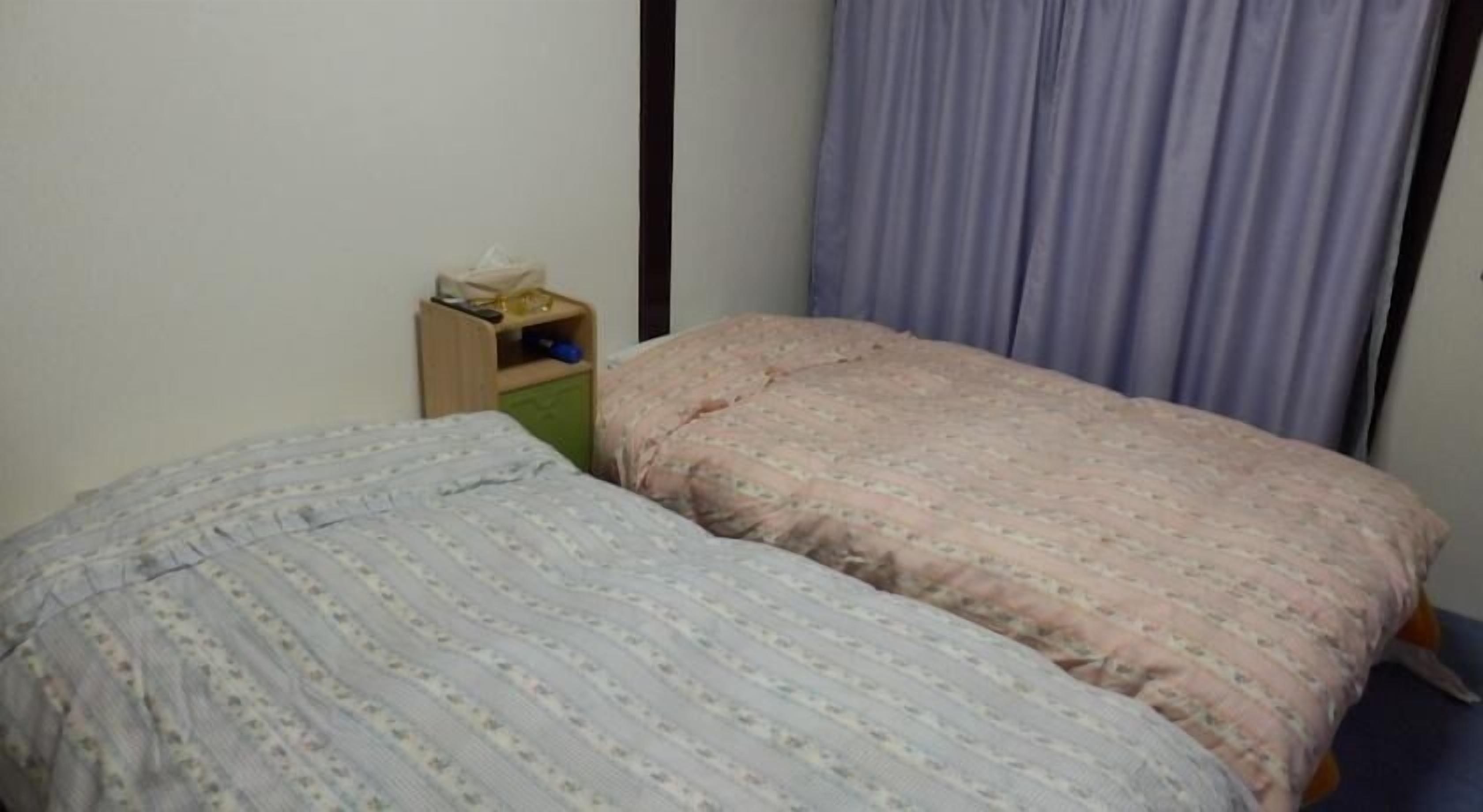 A bedroom with two beds, a wooden nightstand, a green cabinet, and a purple curtain.