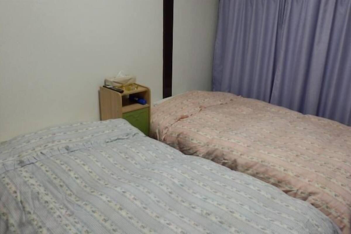 Ein Schlafzimmer mit zwei Betten, einem Holz-Nachttisch, einem grünen Schrank und einem violetten Vorhang.