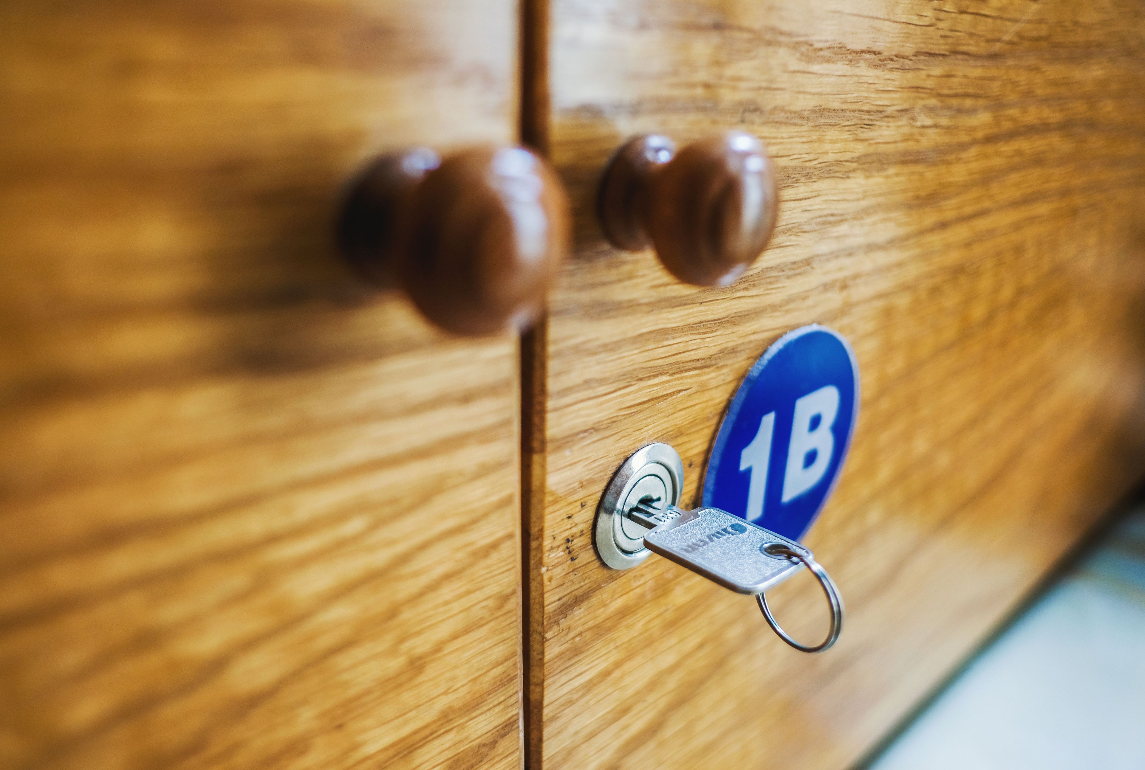 Una puerta de madera con una cerradura y una llave, y un letrero azul con el número "1B".