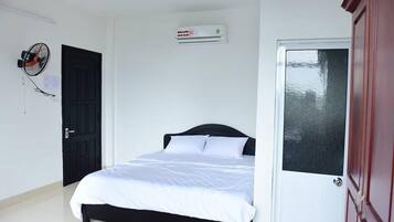 Un dormitorio con cama, aire acondicionado, una puerta y un ventilador de pared.