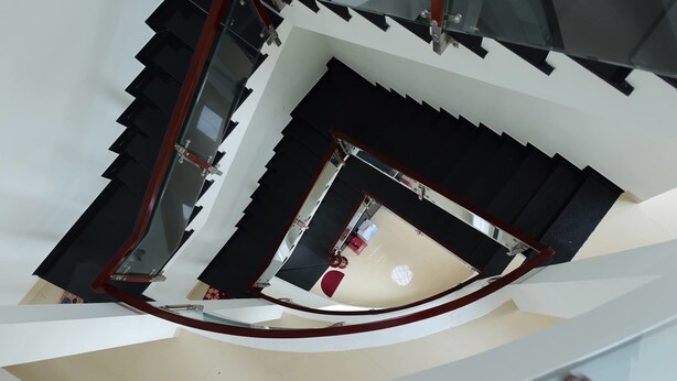 Uma escadaria em espiral com degraus pretos e paredes brancas, descendo para um nível inferior.