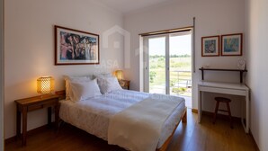 Ein Schlafzimmer mit Bett, Nachttischlampen, einem Schreibtisch und Blick durch eine Schiebetür.