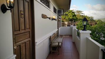 Un balcón estrecho con puerta de madera, un banco y luces fijadas a la pared.