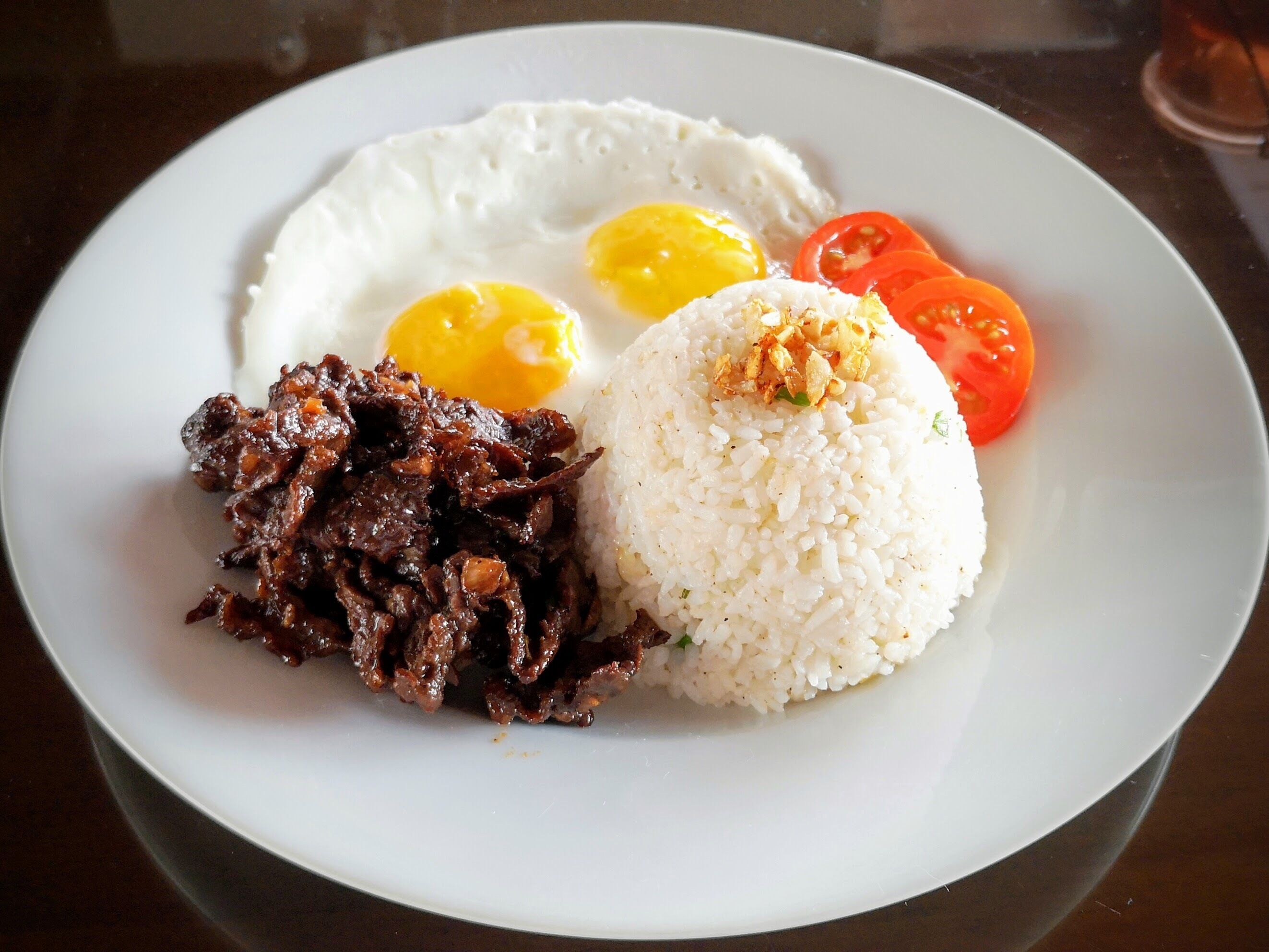 Un plato con arroz blanco, huevos fritos y una guarnición de carne.
