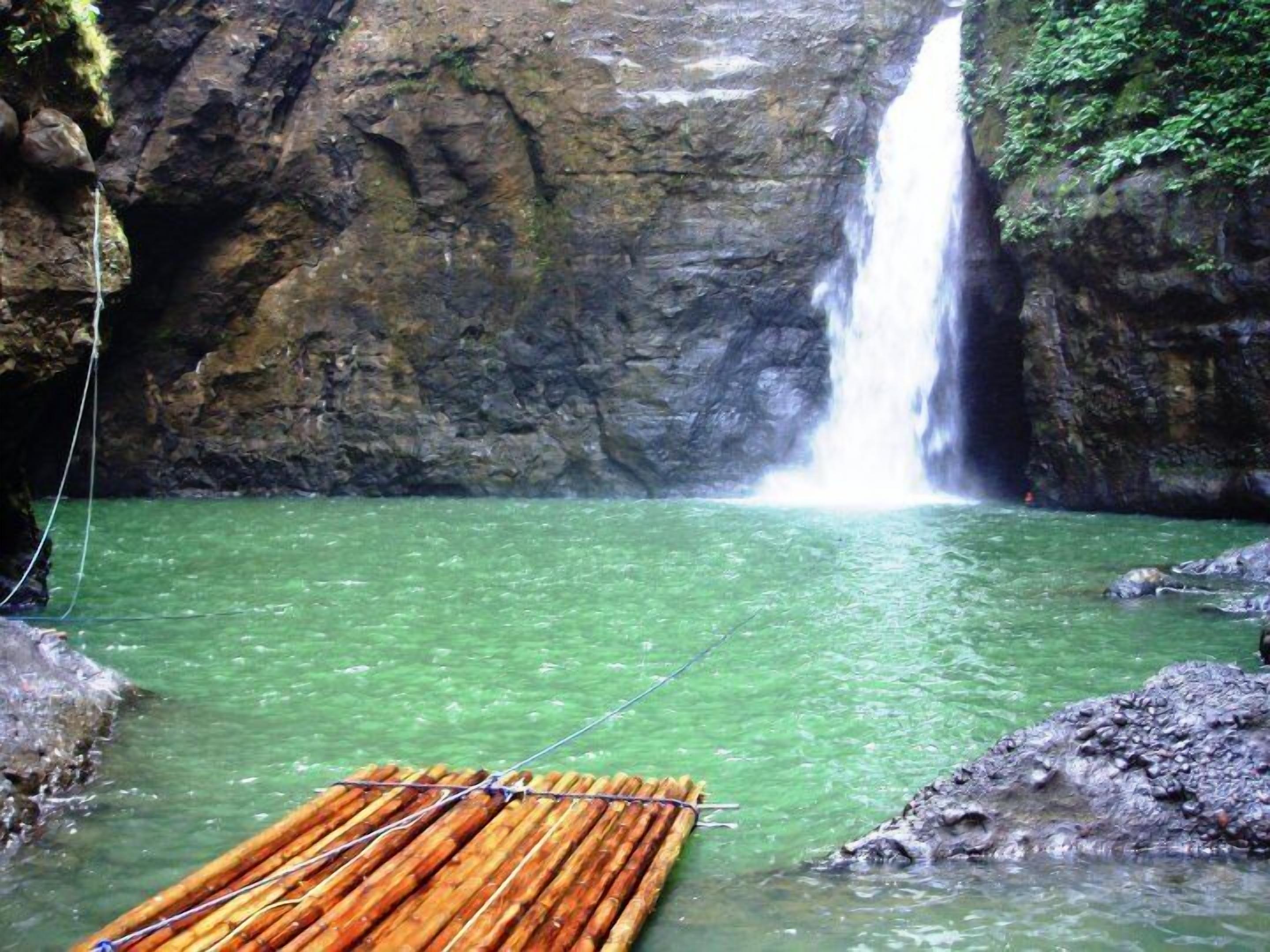 A waterfall in a natural setting with clear water and a bamboo raft.