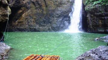 A waterfall in a natural setting with clear water and a bamboo raft.
