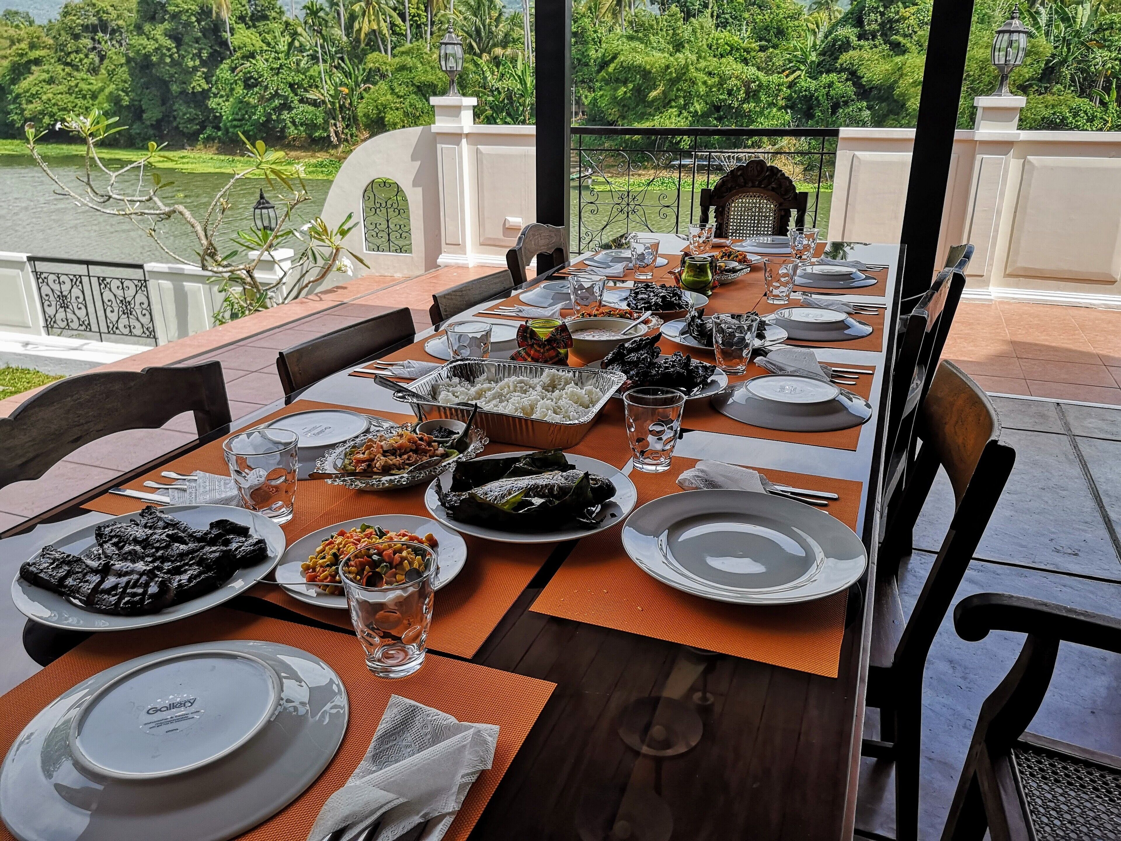 A table set for a meal with various dishes, glasses, and a view of a lake and greenery.