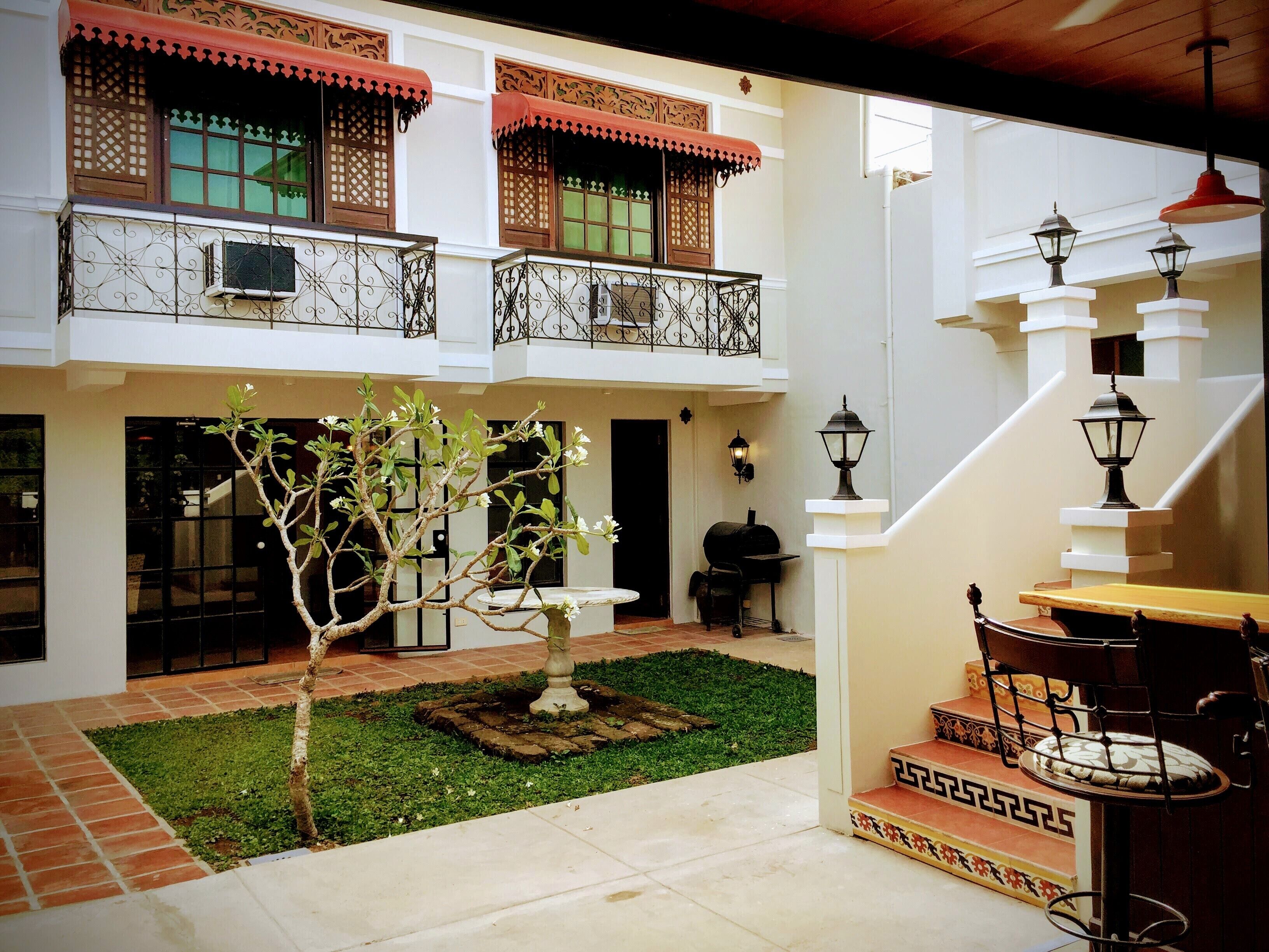 A courtyard with a small tree, a fountain, and a barbecue grill.