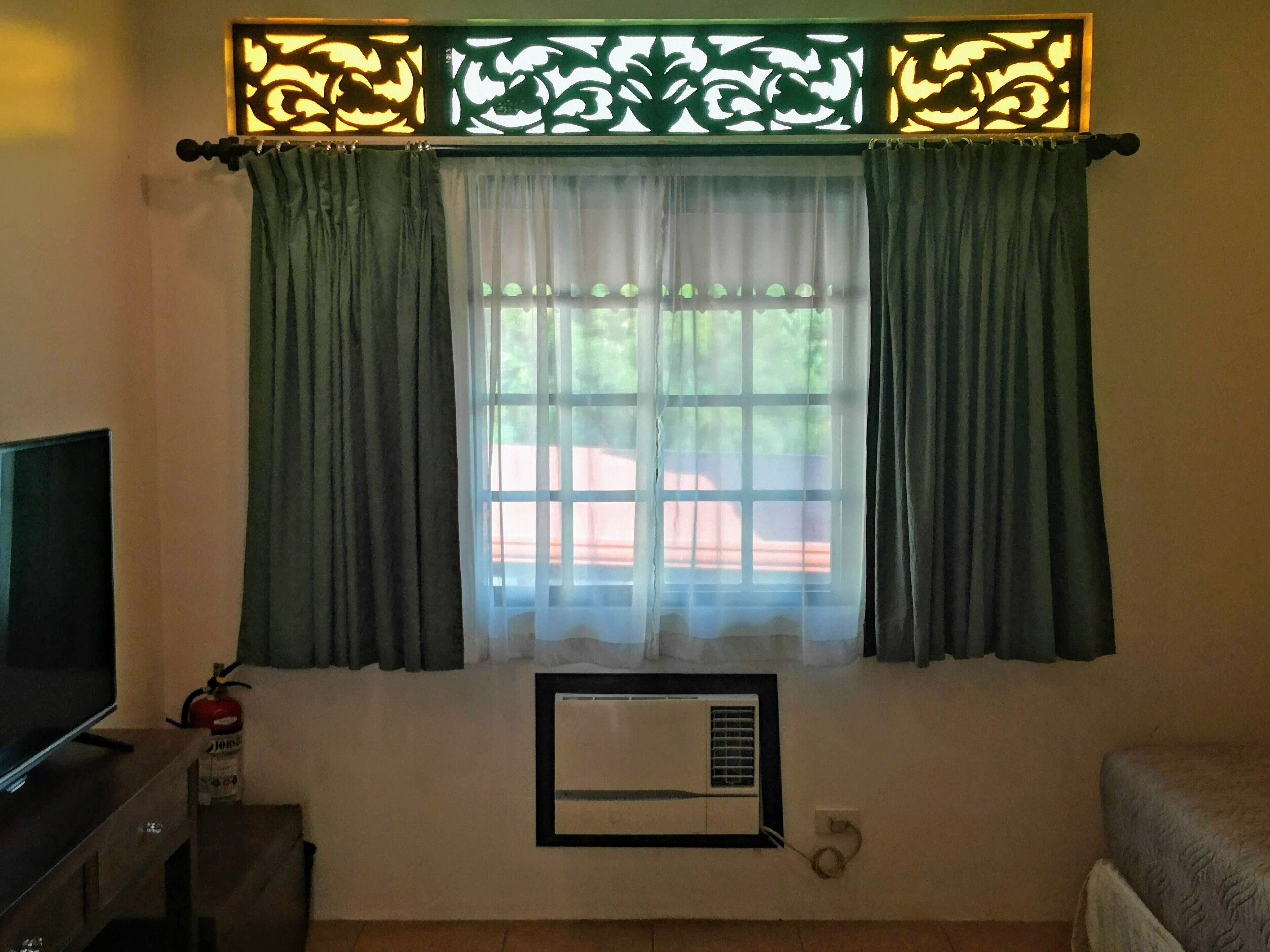 Una habitación con ventana, cortinas, televisión, extintor y aire acondicionado.