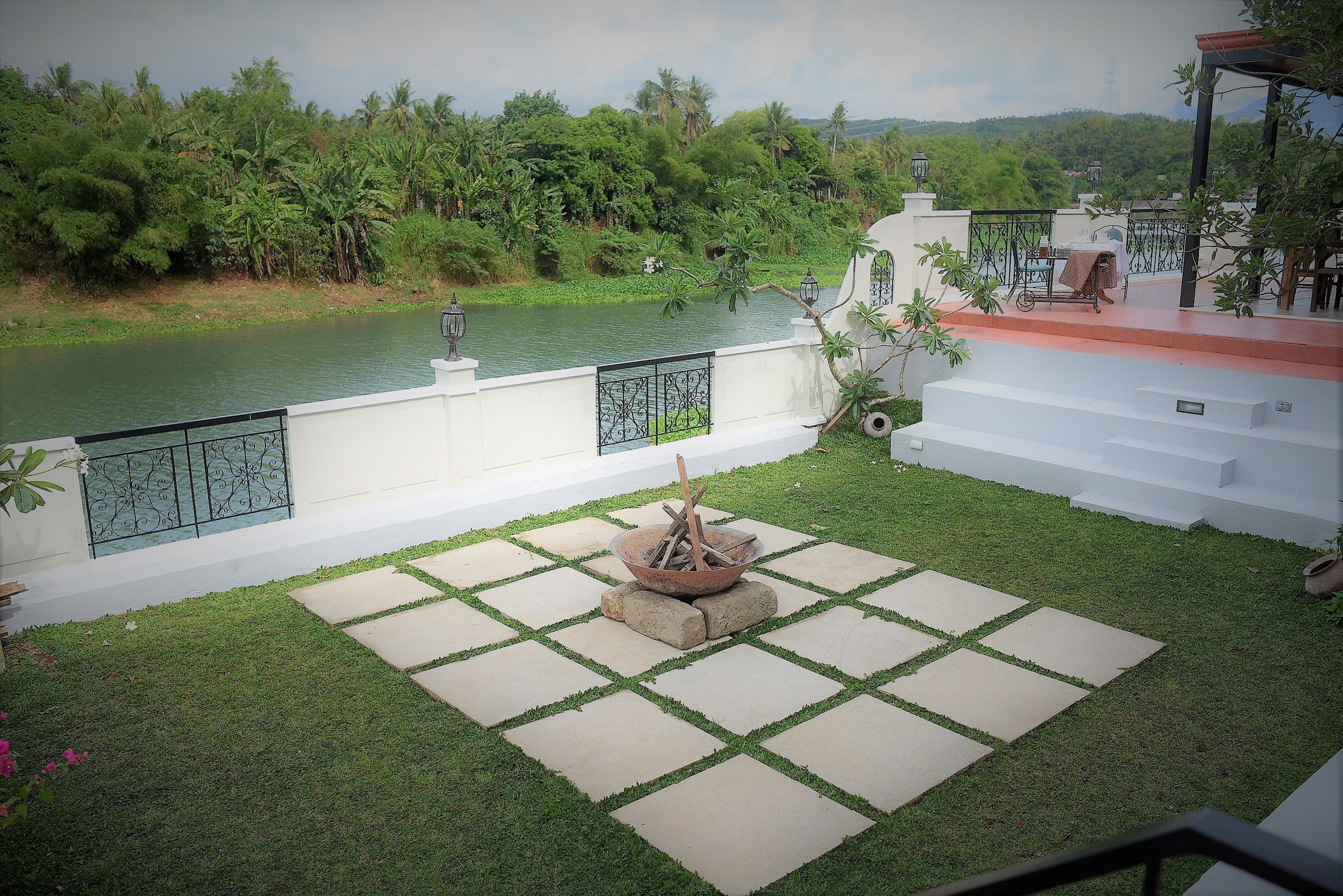 A courtyard with a fire pit, a view of a river, and a white building with a balcony.