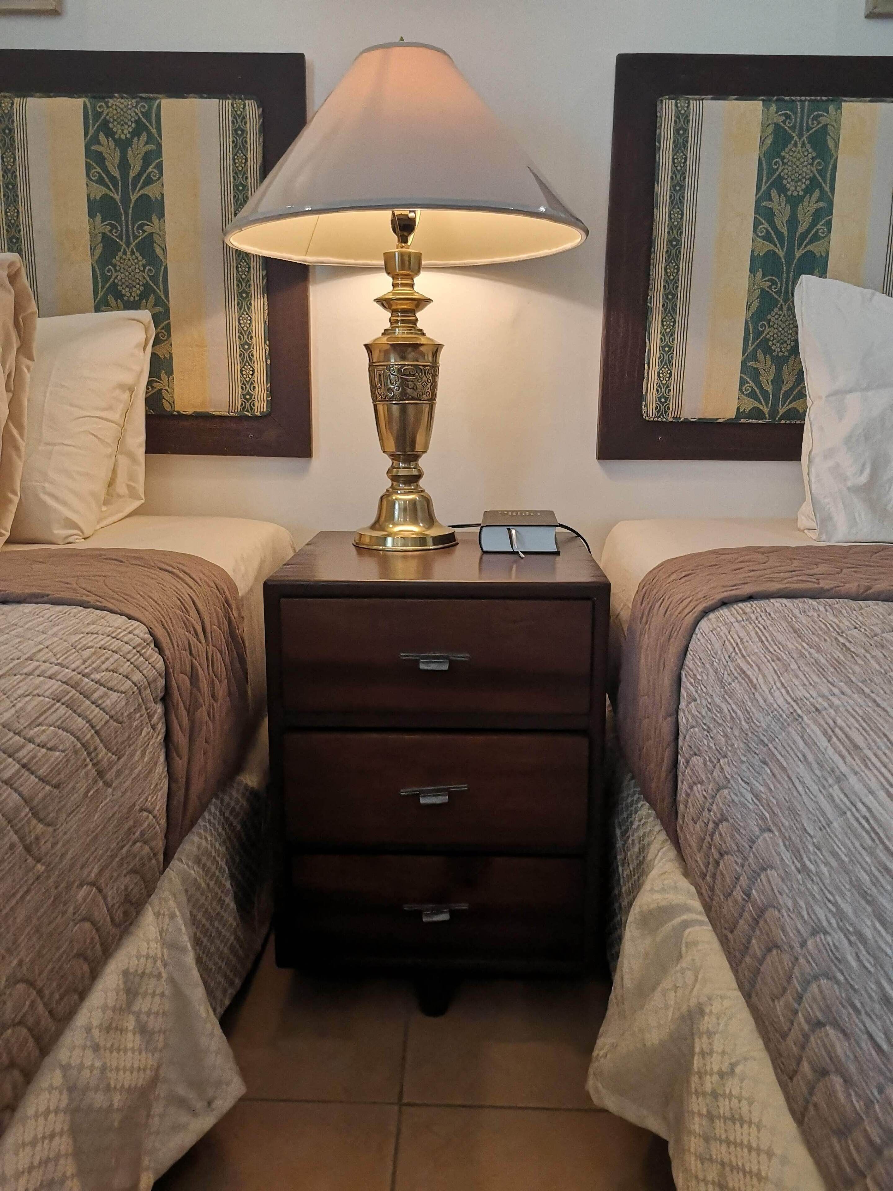Ett hotellrum med två sängar, ett sängbord med en lampa och ett litet bord vid sängen med en telefon och en bok.