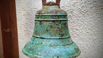 Eine große, verwitterte Glocke mit rustikalem Aussehen, die an einem hölzernen Pfosten befestigt ist.