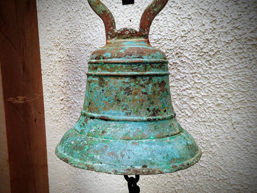 Eine große, verwitterte Glocke mit rustikalem Aussehen, die an einem hölzernen Pfosten befestigt ist.