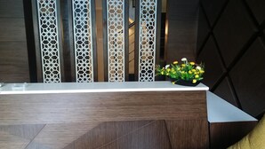A reception desk with a modern design, featuring a wooden finish and a geometric pattern on the back wall. - Sand Silver Business Hotel (Chennai)