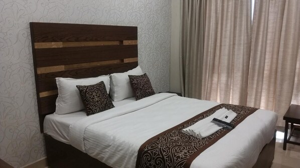 A neatly made bed with a wooden headboard, white bedding, patterned pillows, and a folded towel on the bed. - Sand Silver Business Hotel (Chennai)