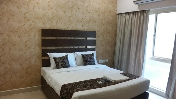 A neatly made bed with white linens and a patterned throw, a dark wooden headboard, and a window with curtains. - Sand Silver Business Hotel (Chennai)