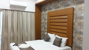A hotel room with a bed, curtains, a patterned wall, and an air conditioning unit. - Sand Silver Business Hotel (Chennai)