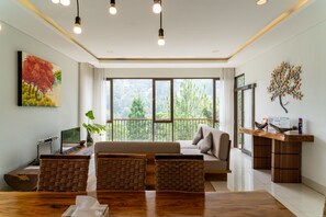 Una sala de estar moderna con un sofá, una mesa de comedor, un televisor y un balcón con vista a árboles.
