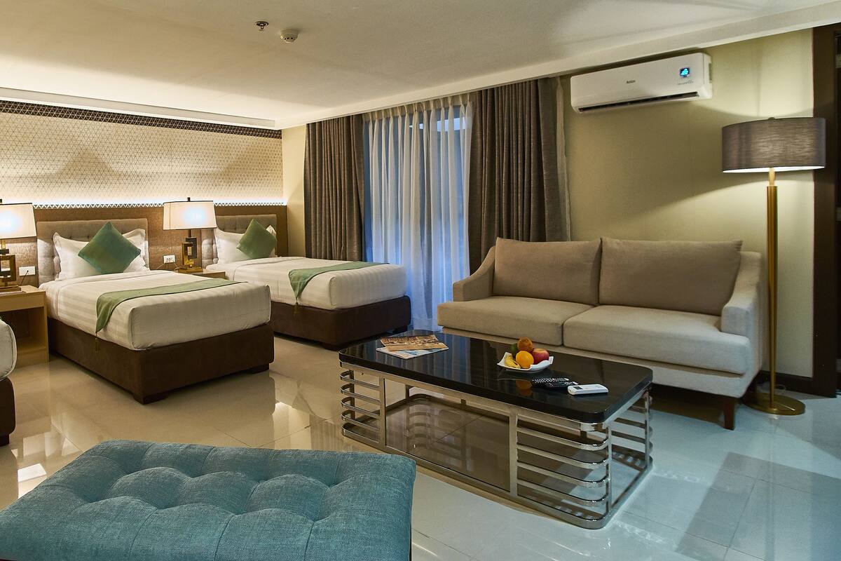 A hotel room with two beds, a sofa, a coffee table, and a lamp.